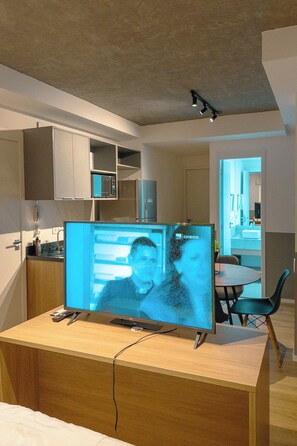 A modern kitchen with built-in appliances, a dining area with a round table and chairs, and a large flat-screen TV on a wooden desk.
