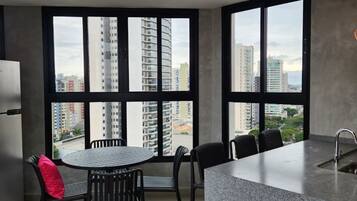 Cozinha moderna com área de jantar, janelas amplas e vista para edifícios altos.