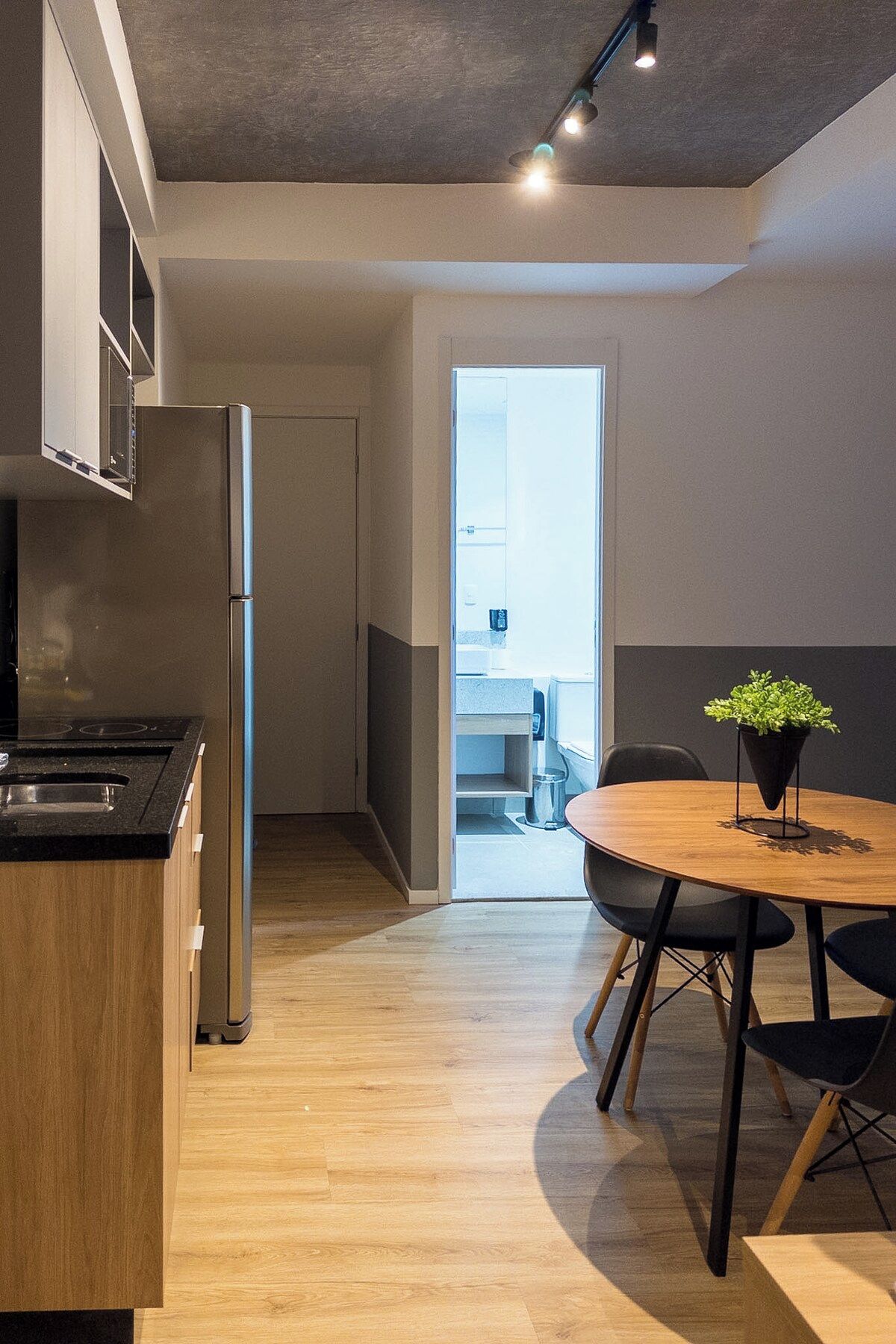 A modern kitchen with a built-in stove, a refrigerator, and a dining area with a round wooden table and black chairs.