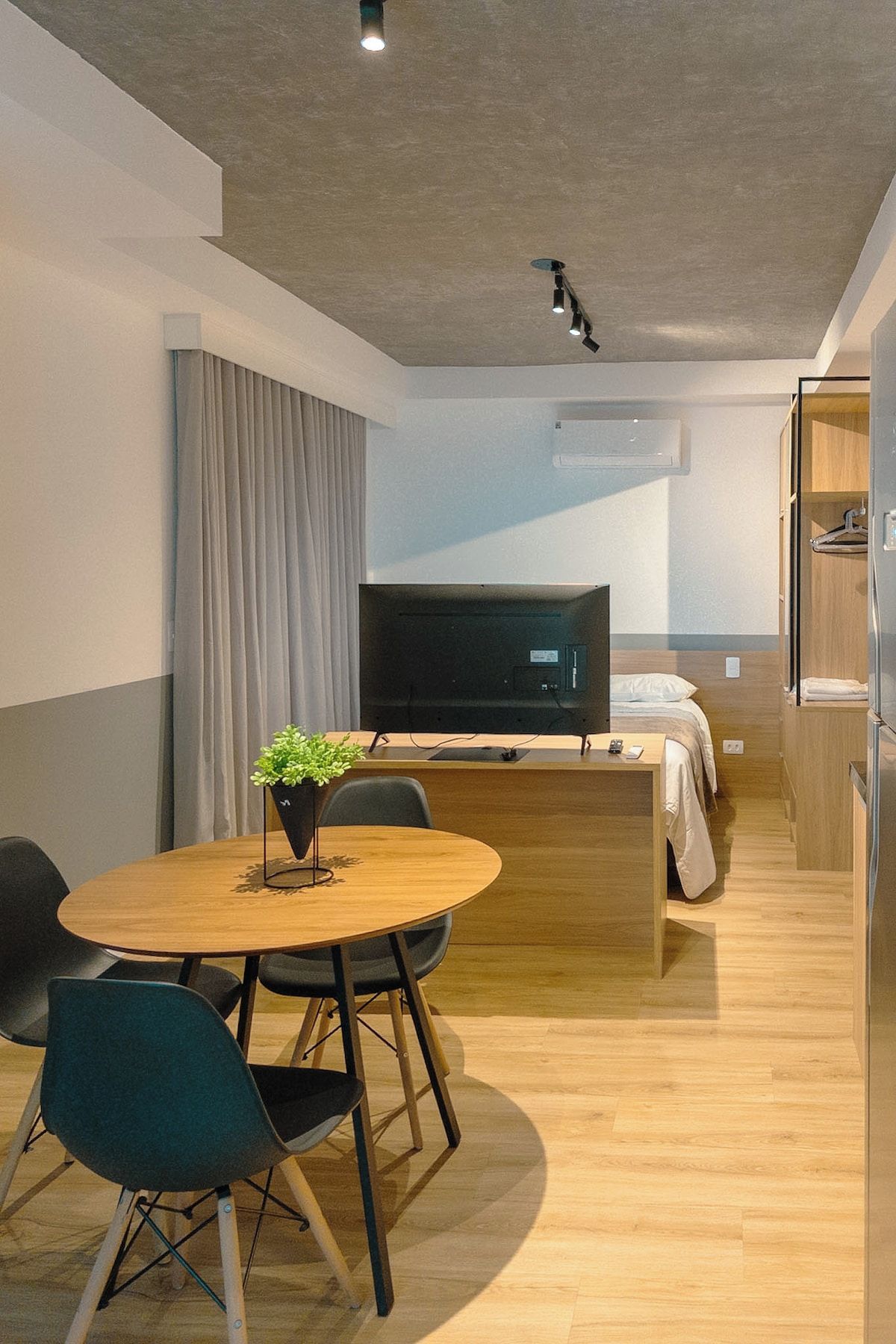 Una habitación de hotel moderna con zona de comedor, cama, televisor y kitchenette.