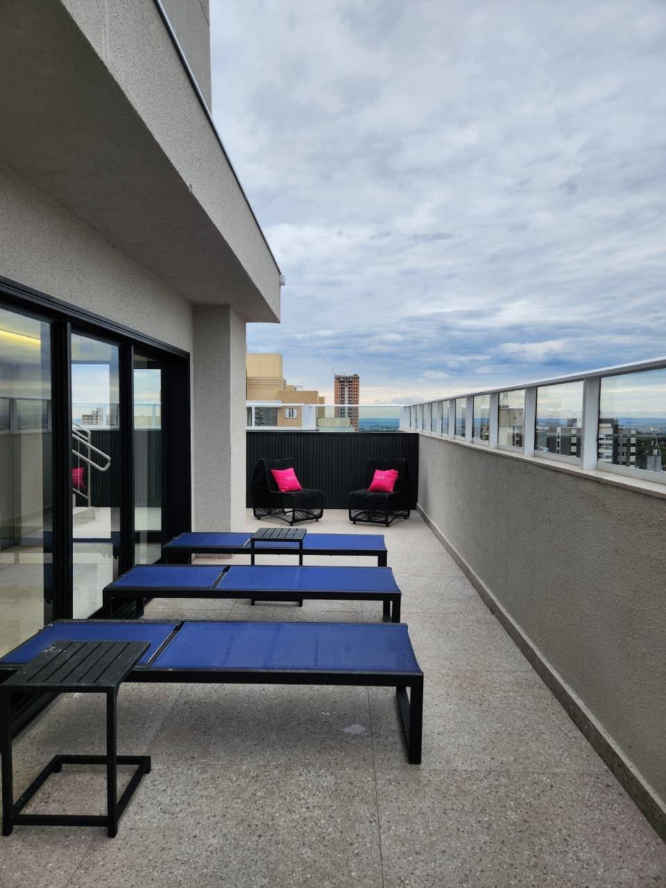 Una terraza al aire libre con mesas y sillas, un acceso por puerta de vidrio y vistas panorámicas de la ciudad.