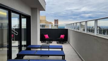 Una terraza al aire libre con mesas y sillas, un acceso por puerta de vidrio y vistas panorámicas de la ciudad.