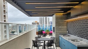 A rooftop terrace with a round table and chairs, a kitchen area with a sink, and a view of buildings in the background. - Private Room with Pool and Gym - BEDEO302B (Maringá)