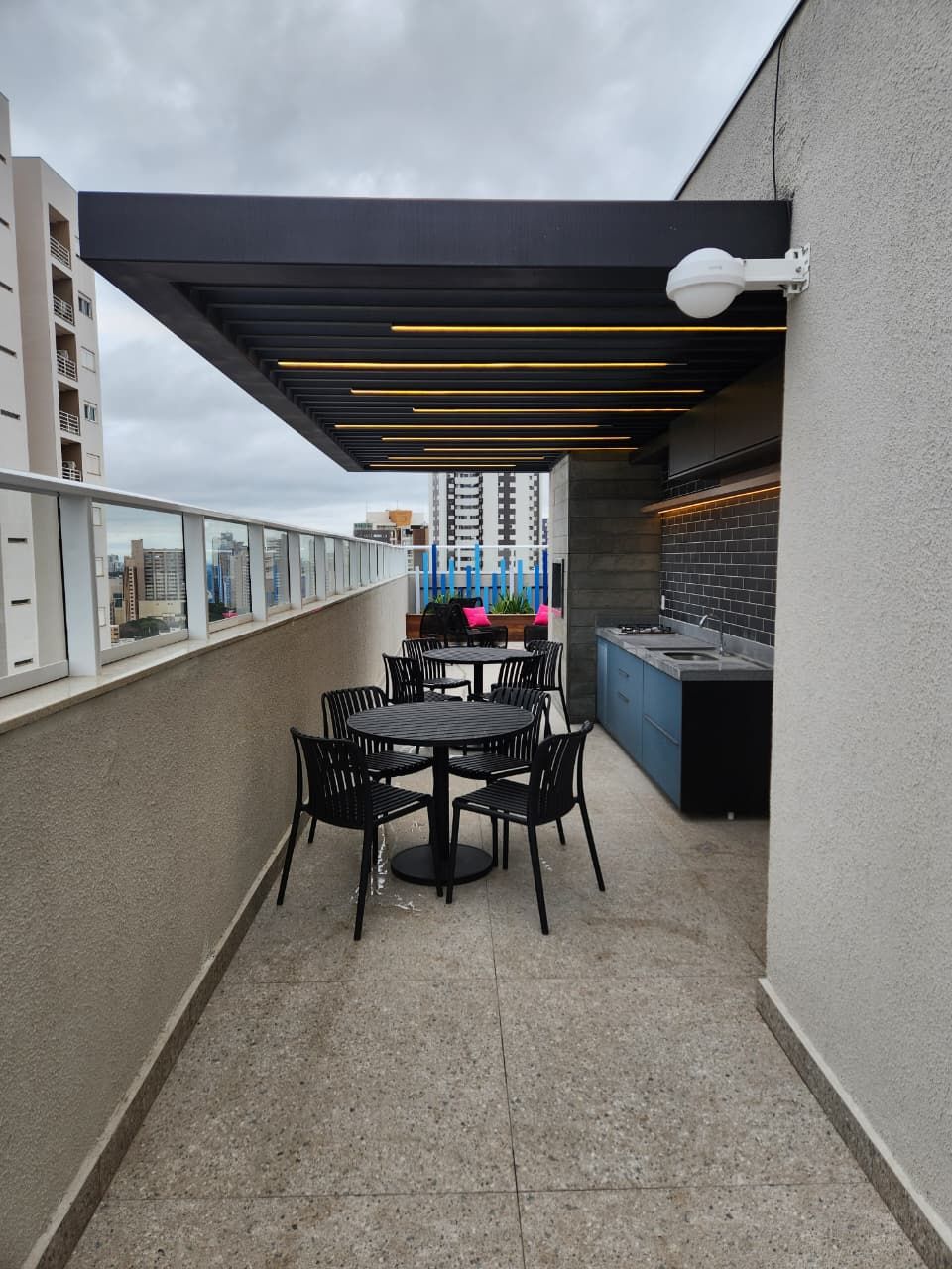 Uma área de refeições ao ar livre com mesa e cadeiras, cozinha e vista para a paisagem urbana.