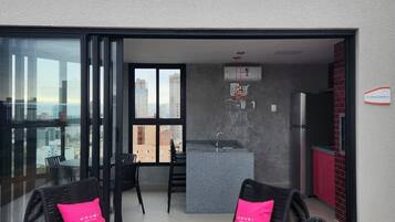 Un appartement moderne doté d’un balcon, d’une cuisine et d’un coin repas avec des meubles en rotin noir et des coussins roses.