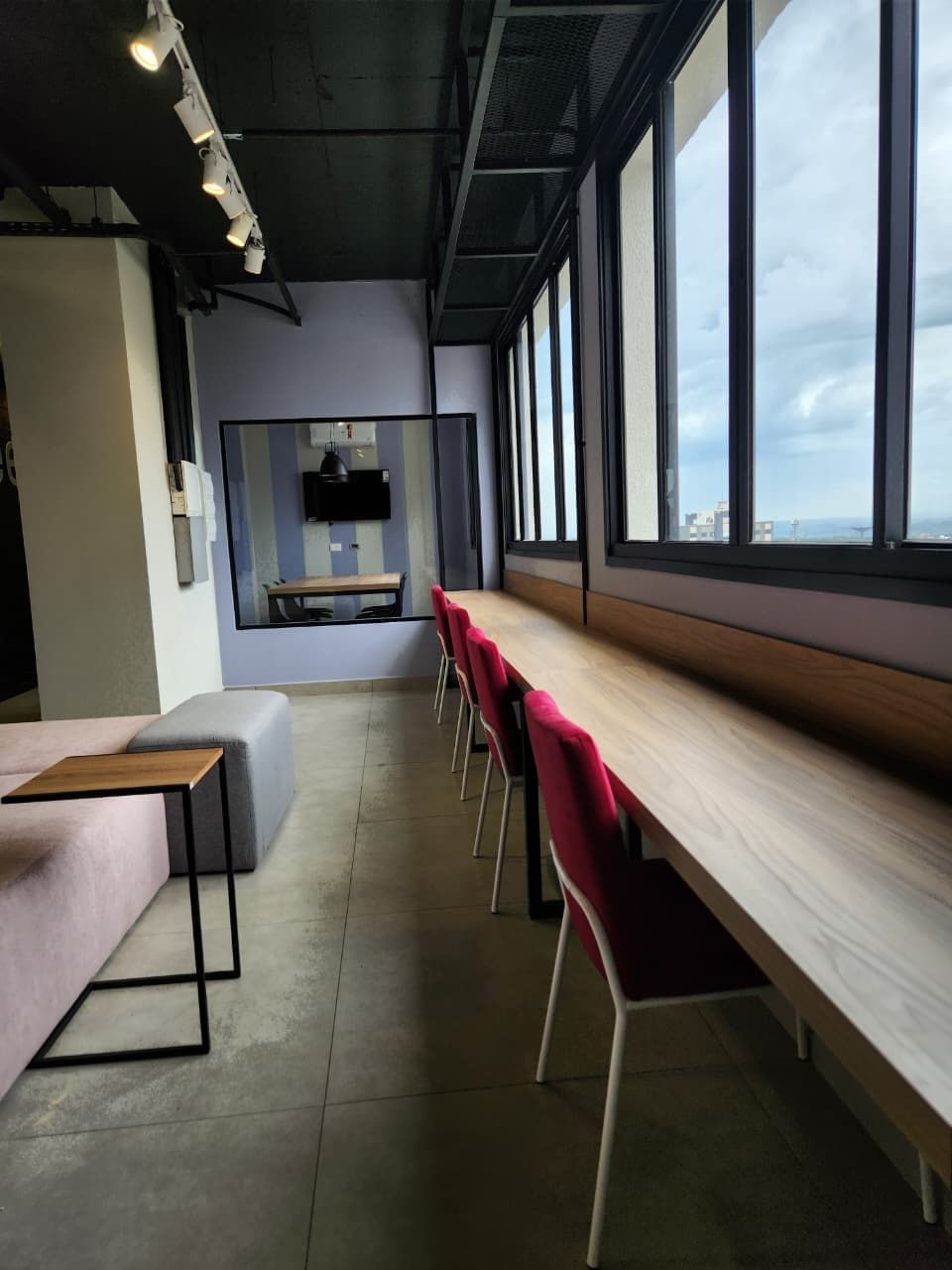 Um interior moderno com uma mesa comprida e cadeiras vermelhas, grandes janelas e um banco.