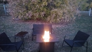 Ein Außenbereich mit Sitzgelegenheit und einem Feuerkorb, umgeben von Stühlen und einem Tisch.