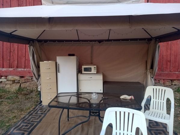 A tented outdoor area with a table, chairs, a refrigerator, and a microwave.