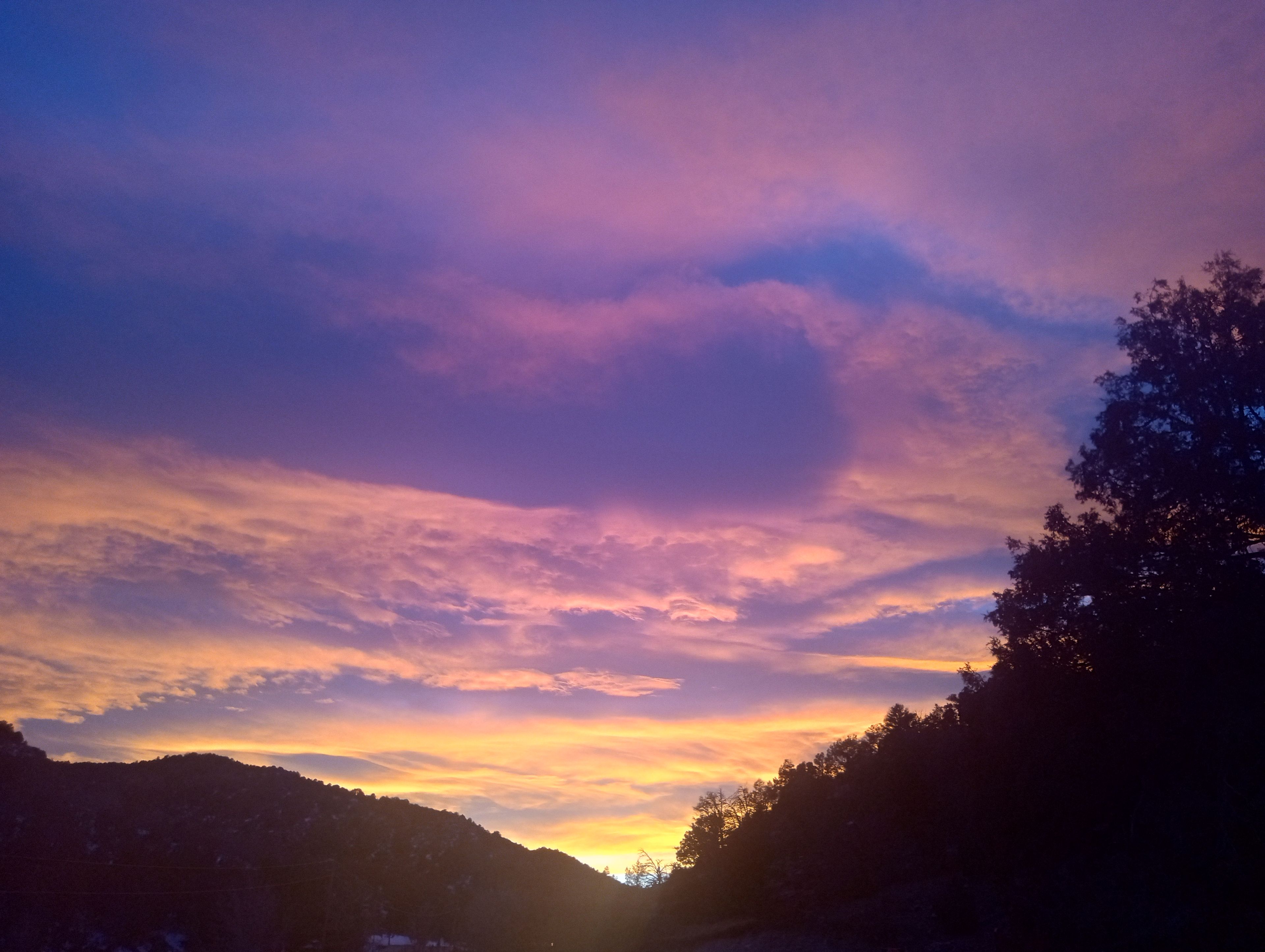 Un atardecer sobre un paisaje montañoso con árboles silueteados contra el cielo.