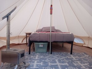 A tent with a bed, a portable heater, and a trash bin.