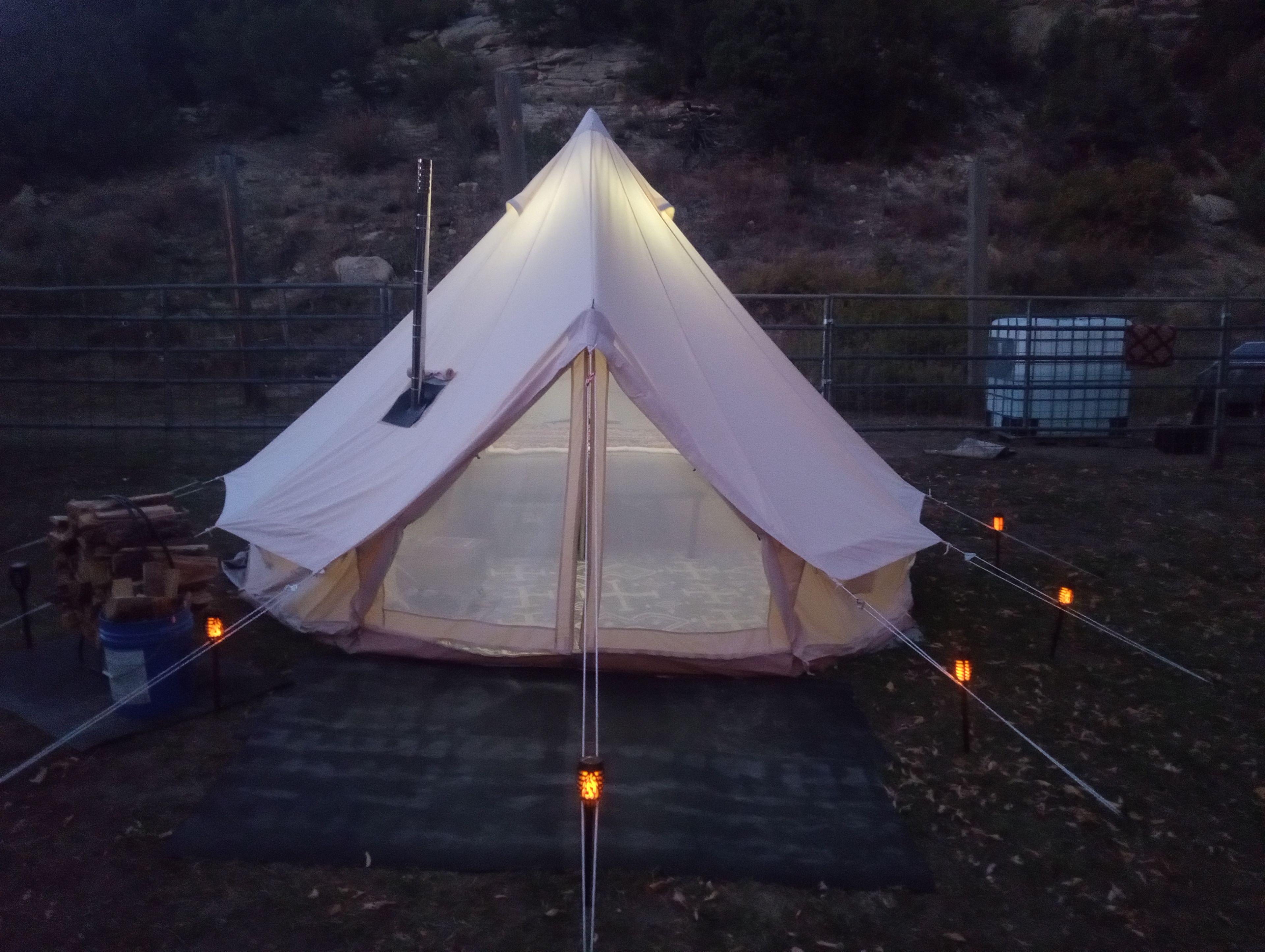 A tent with a peaked roof, surrounded by a fence, and a basketball hoop in the background.
