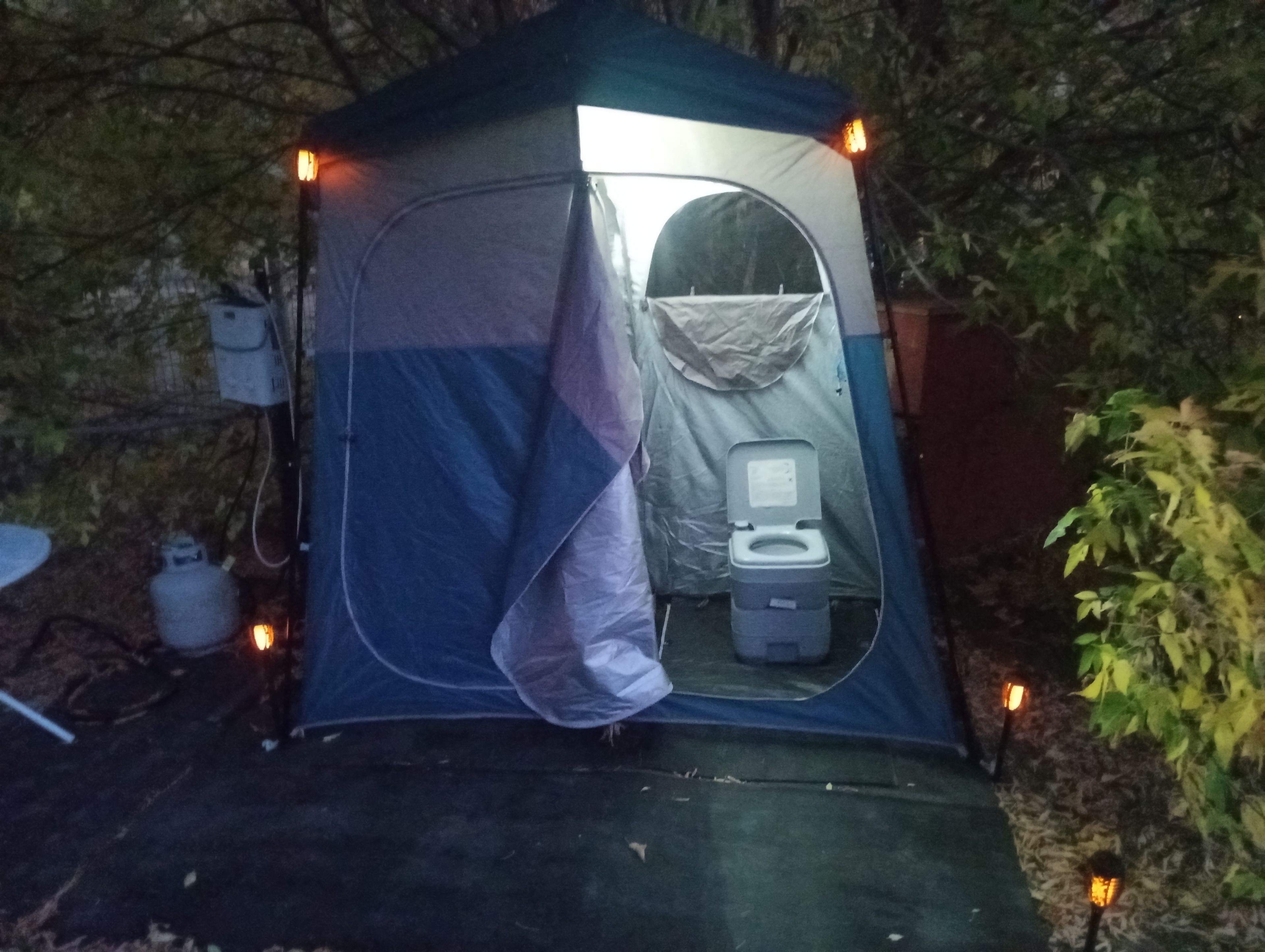 Una carpa con un baño químico portátil, rodeada de árboles.