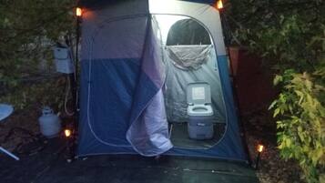 Una carpa con un baño químico portátil, rodeada de árboles.