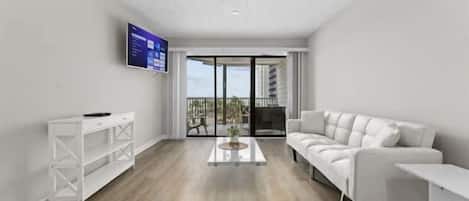 A modern living room with a white sofa, a coffee table, and a TV mounted on the wall.