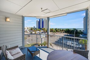 A balcony with wicker furniture, a view of the street, and a building in the background. - New Oceanview Suite Bluewater Villas with Pools (Myrtle Beach)