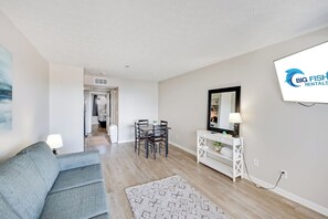A modern living room with a sofa, a dining table with chairs, a white console table with a lamp, and a large mirror on the wall. - New Oceanview Suite Bluewater Villas with Pools (Myrtle Beach)