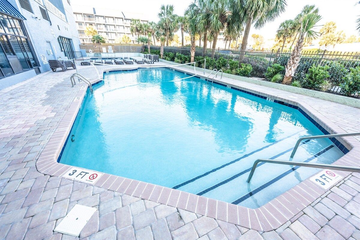 A rectangular swimming pool with a 3-foot depth marker, surrounded by a brick deck and palm trees.