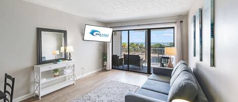 A modern living room with a sofa, a TV, a console table, and a view of the ocean.