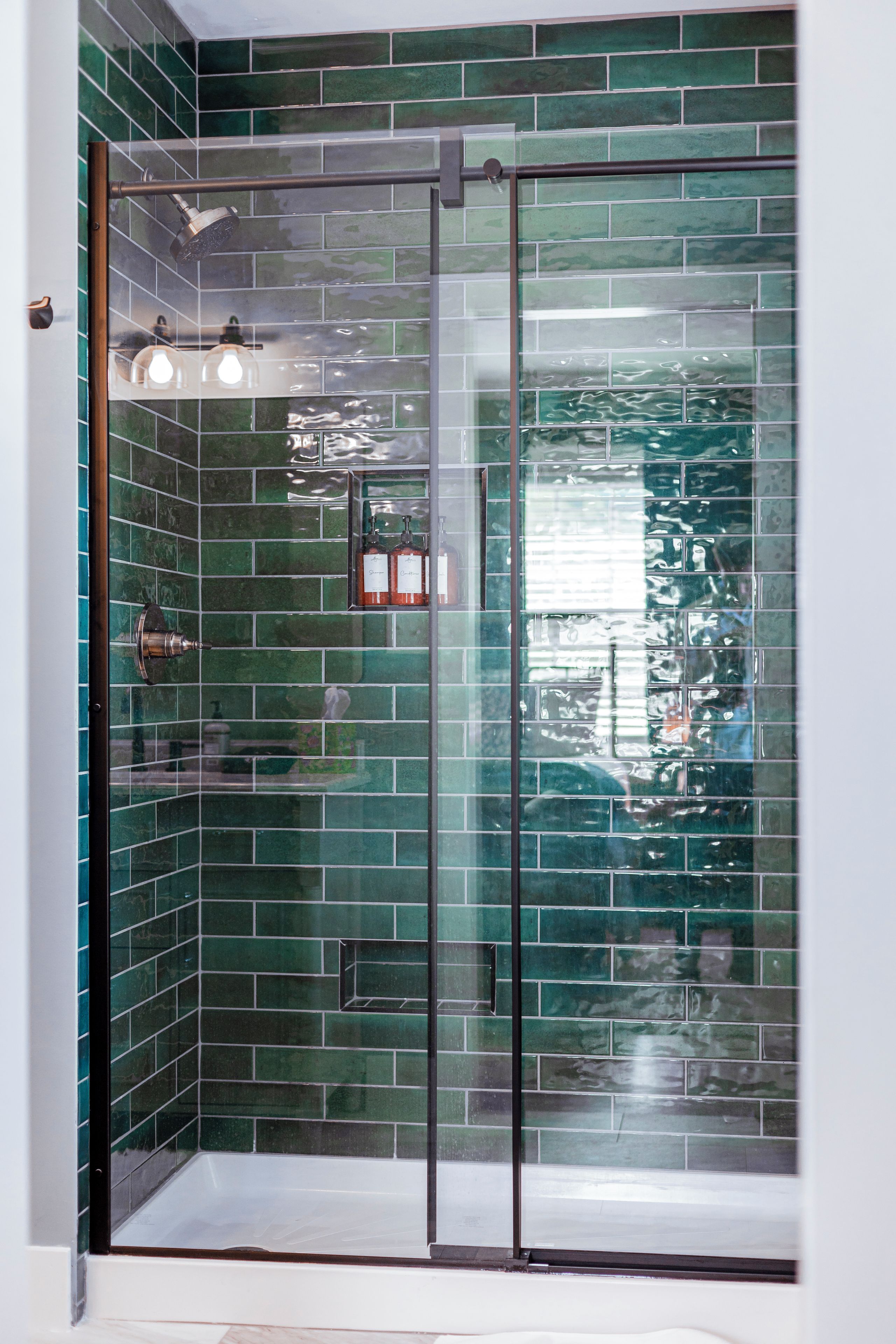 A glass-enclosed shower with green-tiled walls and a visible reflection of a building outside.