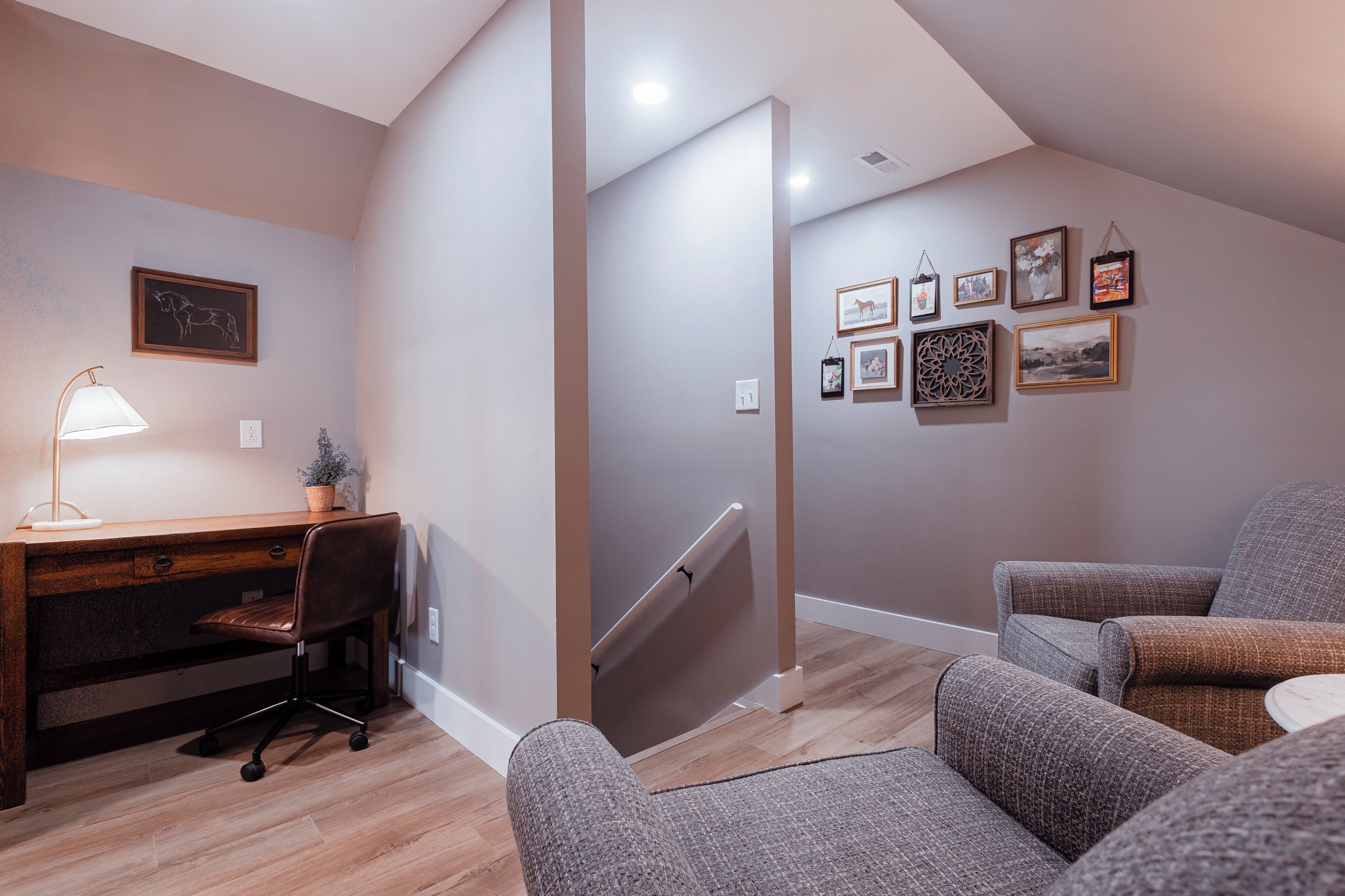 A modern interior with a desk, office chair, and two armchairs. A staircase leads to an upper level.