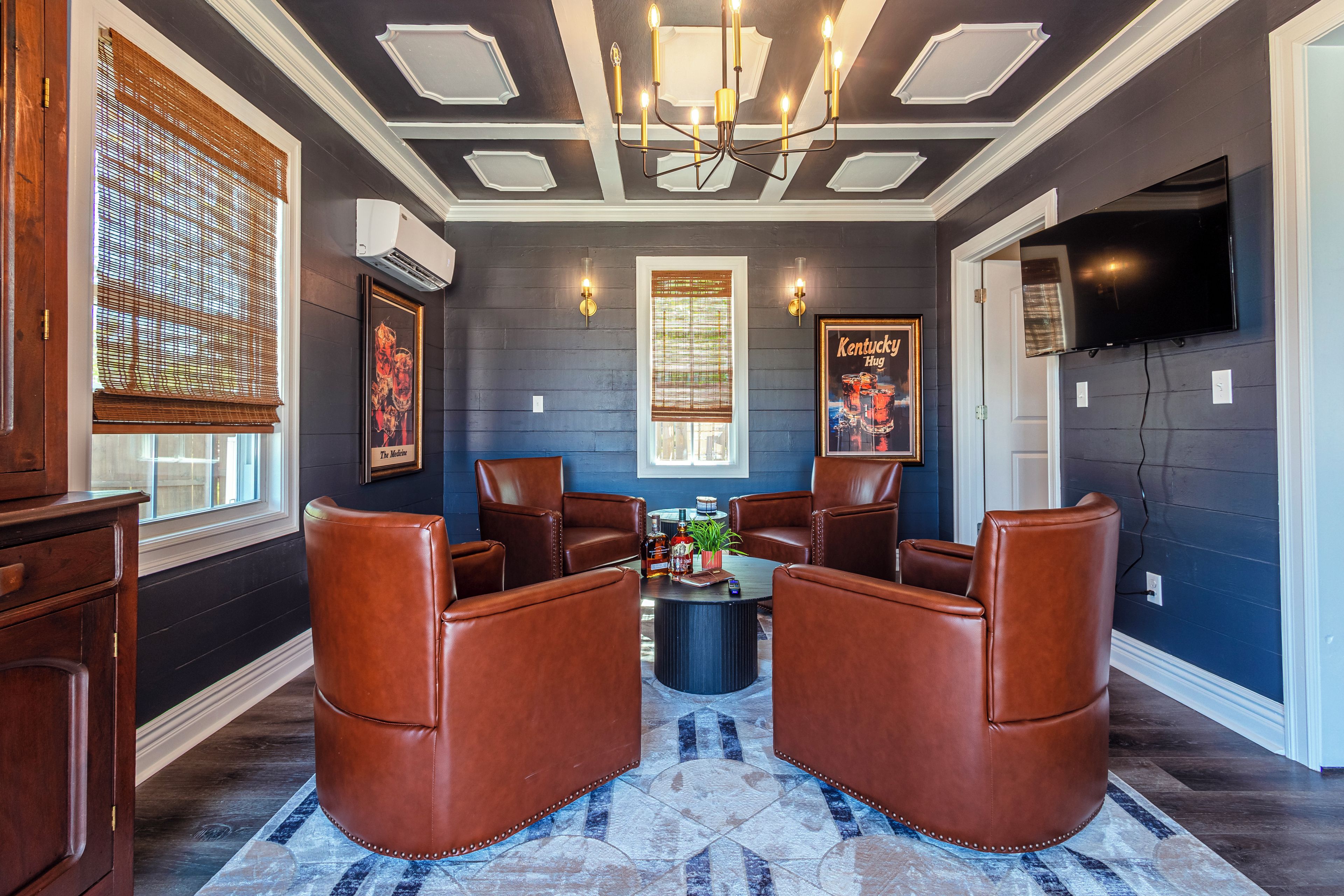 A room with a dark blue wall, a chandelier, leather chairs, a coffee table, and a poster.