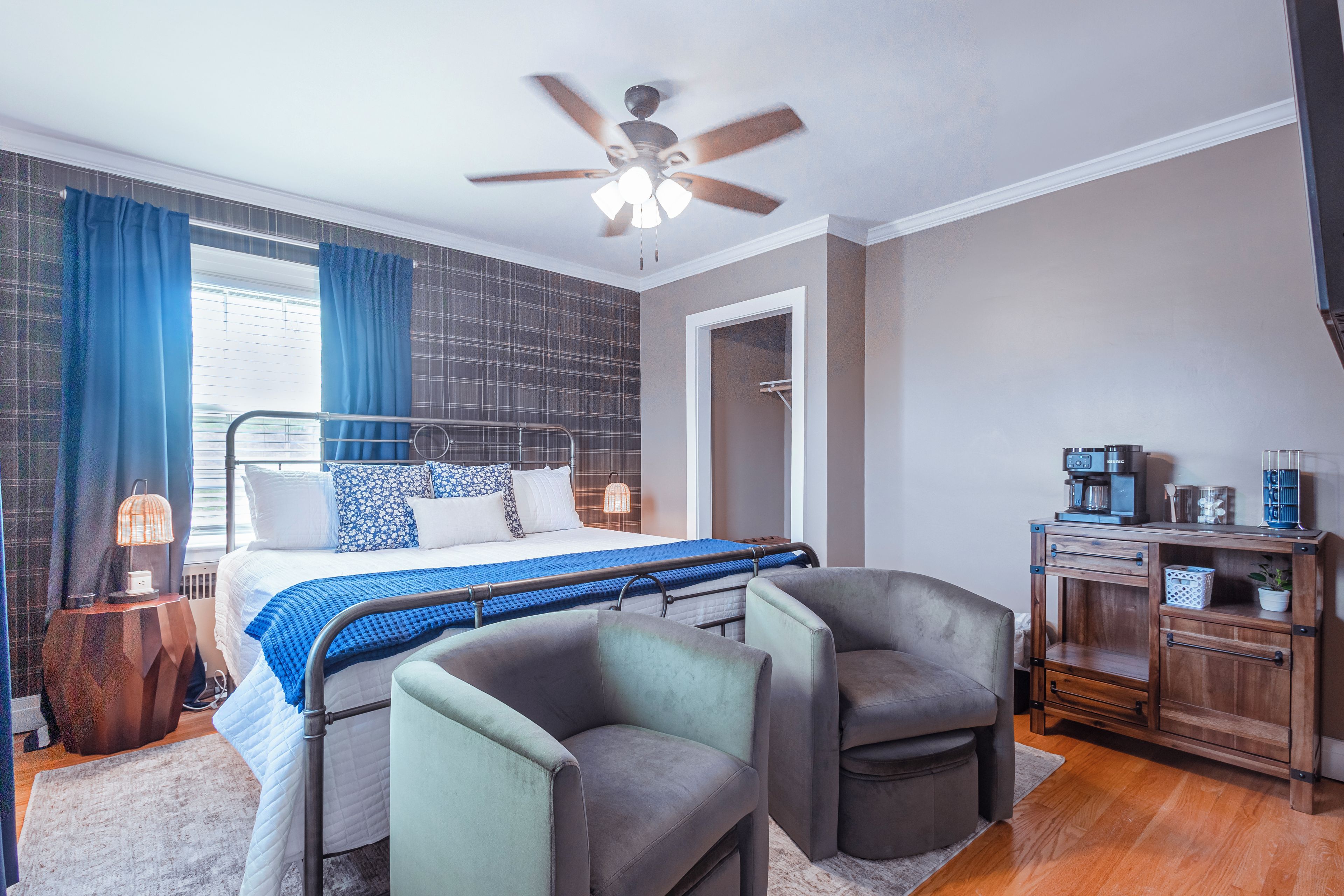 A modern bedroom with a bed, two armchairs, a coffee machine, and a nightstand.