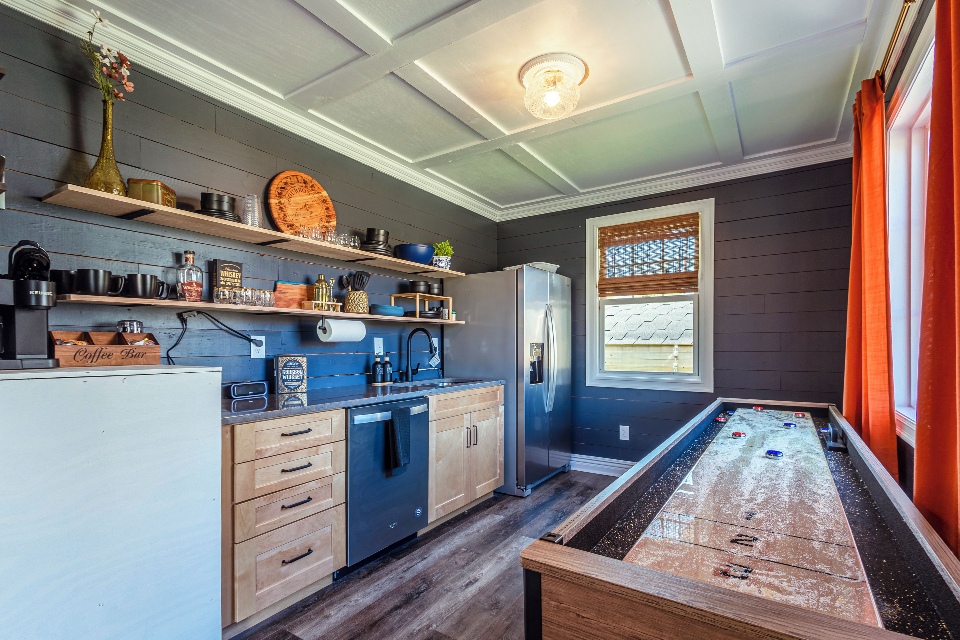 Una cocina con armarios de madera, un refrigerador, una cafetera y una mesa de futbolín.