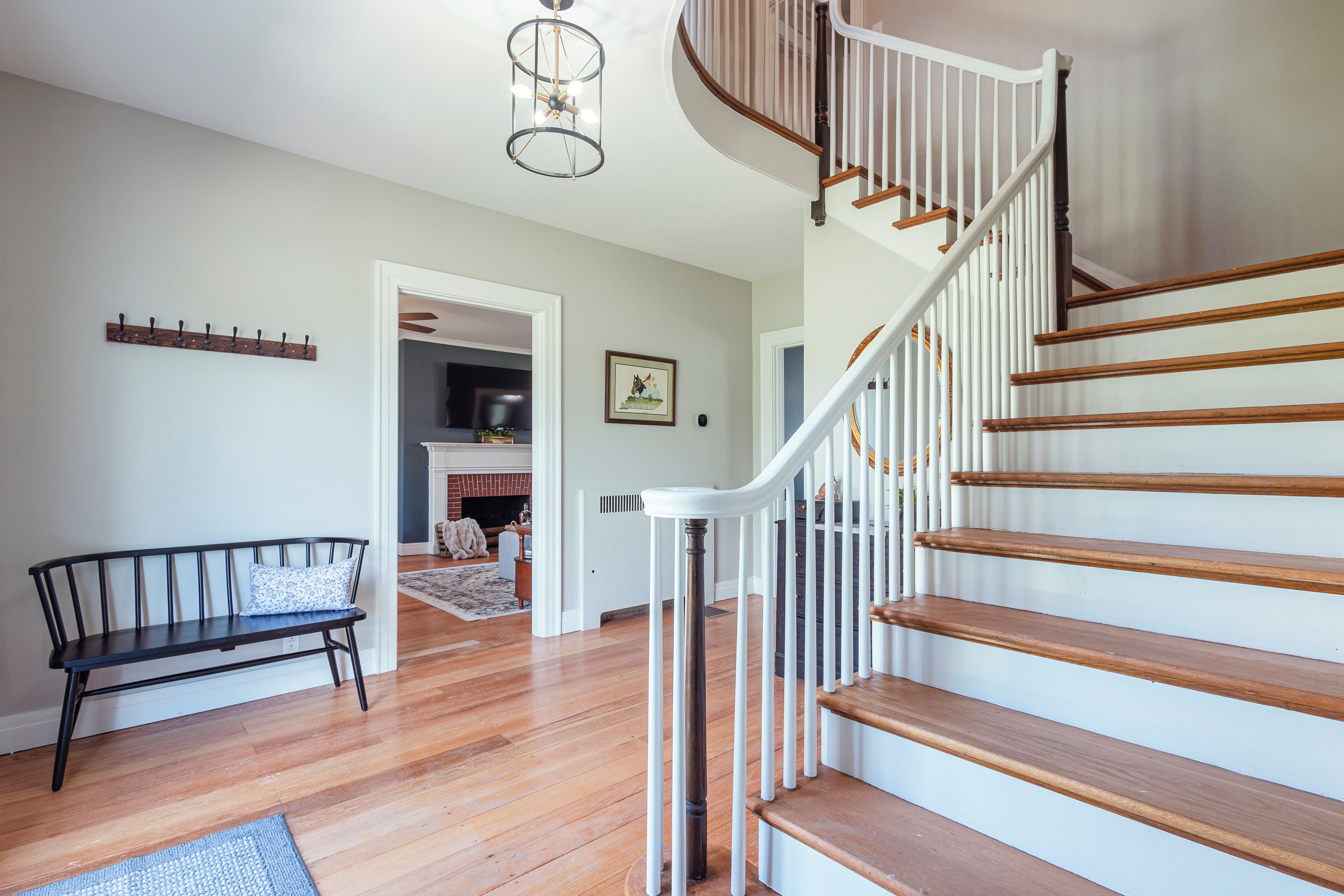 A staircase with wooden steps and white railings, a bench with a cushion, a coat rack, and a hanging light fixture.