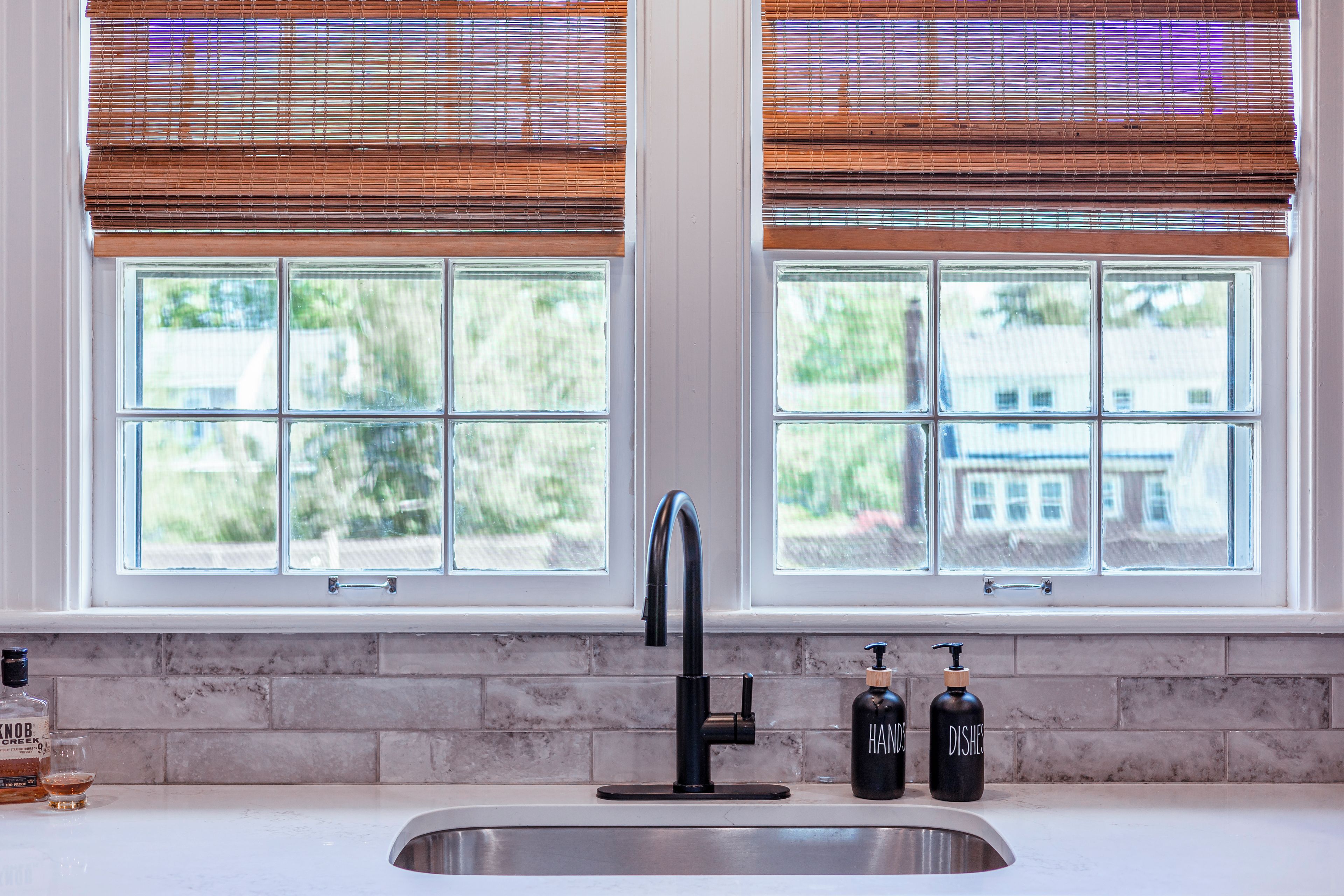 A kitchen with a stainless steel sink, two bottles labeled 'HAND' and 'DISHES', and a bottle of whiskey.