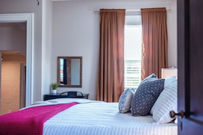 Quarto de hotel com cama, escrivaninha, cadeira, espelho e janela com cortinas.