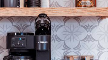 Una macchina da caffè Keurig su un bancone della cucina, con una caraffa, un barattolo di biscotti e un cucchiaio di legno.