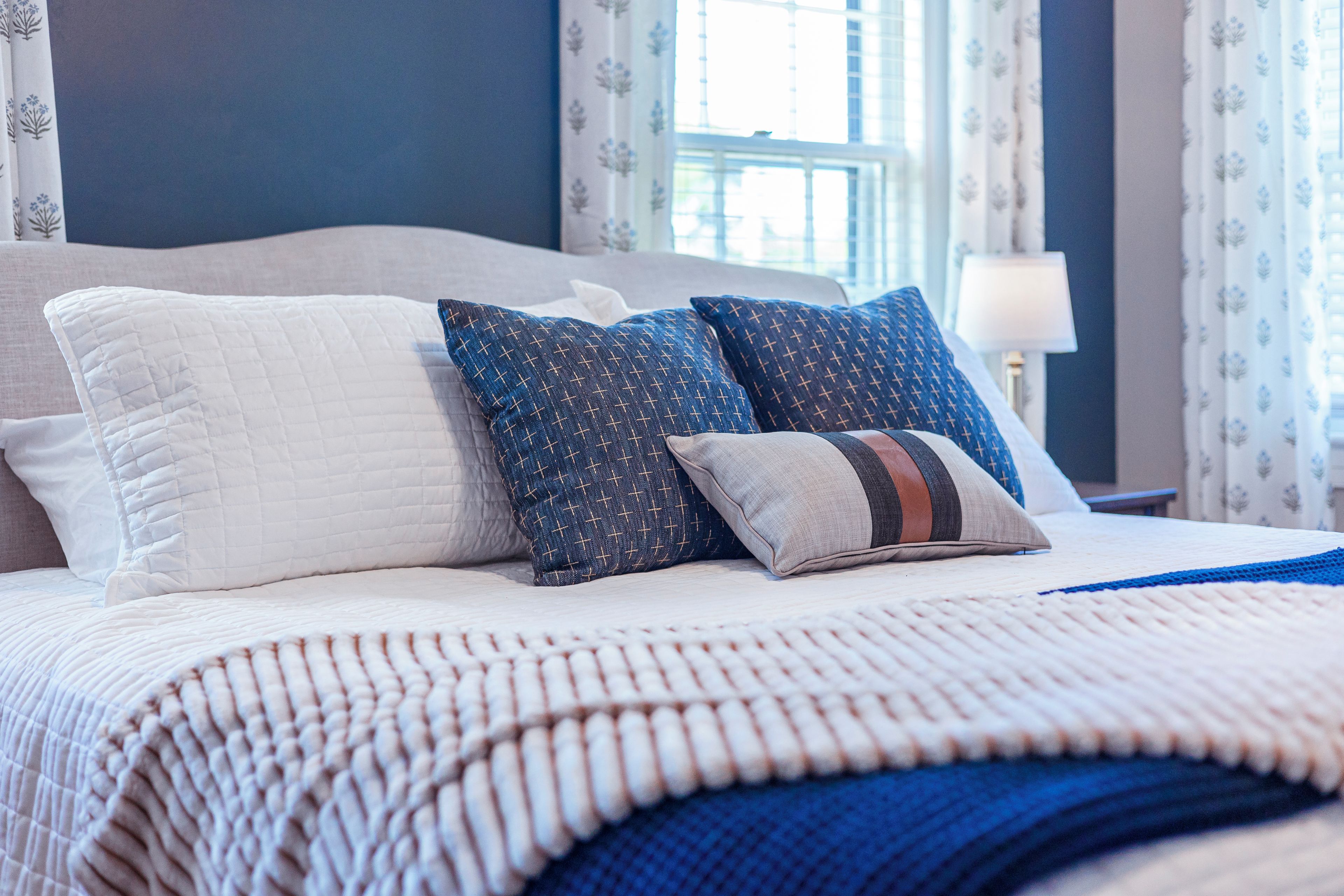 A neatly made bed with a white quilt, two patterned pillows, and a blue throw blanket.