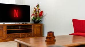 Ett vardagsrum med en tv-apparat som visar Netflix-logotypen, ett träfärgat mediacentrum, en röd fåtölj och en prydnadsväxt.