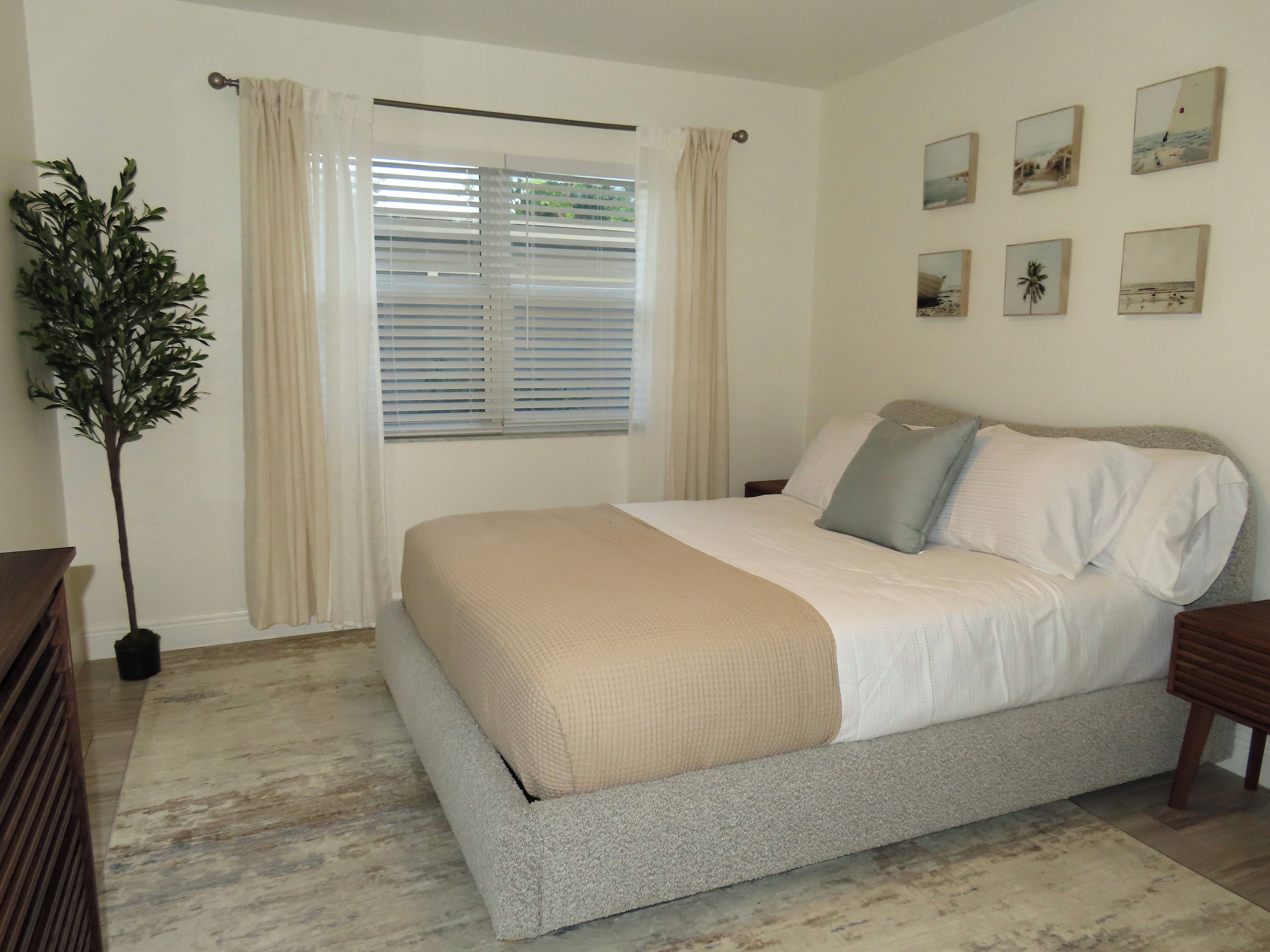 A bedroom with a bed, curtains, a potted plant, and wall art.