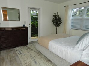 A bedroom with a bed, a dresser, a door leading to a garden, and a window with blinds. - Linen and Palm 1bed/1bath heart of Fort Lauderdale (Fort Lauderdale)
