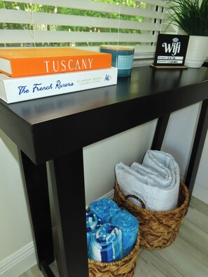 Een tafel met een boek getiteld 'Tuscany', een 'WiFi' bordje, een kaars en een mand met opgevouwen handdoeken.