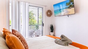 A bedroom with a bed, a TV on the wall, a balcony with a view, and a potted plant.