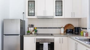 A modern kitchen with white cabinets, a stainless steel refrigerator, a dishwasher, and a coffee maker.