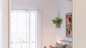Ein Zimmer mit großem Fenster, einer hängenden Pflanze und einem gerahmten Kunstwerk an der Wand.