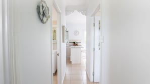 A hallway leading to a kitchen with white cabinetry and a clock on the wall.
