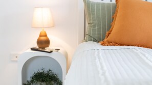 Ein ordentlich gemachtes Bett mit weißer Bettwäsche und einem einzelnen orangefarbenen Zierkissen.