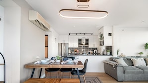 Une cuisine moderne avec des meubles blancs, un îlot central et un coin repas comprenant une table et des chaises en bois.