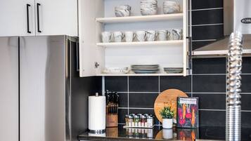 Una cocina con un refrigerador de acero inoxidable, gabinetes blancos, salpicadero de azulejos negros y un libro titulado 'VEGETABLES' sobre el mostrador.