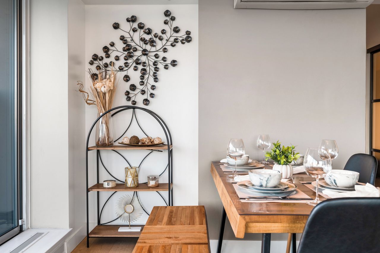 A dining area with a wooden table set for four, a metal wall art piece, and a decorative shelf with various items.