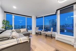 Un salon moderne avec un canapé, des fauteuils et de grandes fenêtres donnant sur la ville.