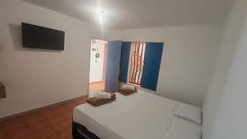 A bedroom with a bed, a flat-screen TV, and a window with blue shutters.