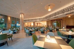 A spacious indoor dining area with multiple tables and chairs, a central pillar, and a mezzanine level with a railing. - Chensheng International Hotel (Zhangjiajie)