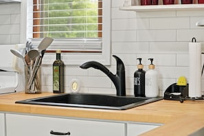 A kitchen with a black sink, white tiles, and various kitchen items on the counter. - Cedar Lake Sunrise: 1BR, 1.5 Bath with Lake View and Back Porch (Cedar Lake)