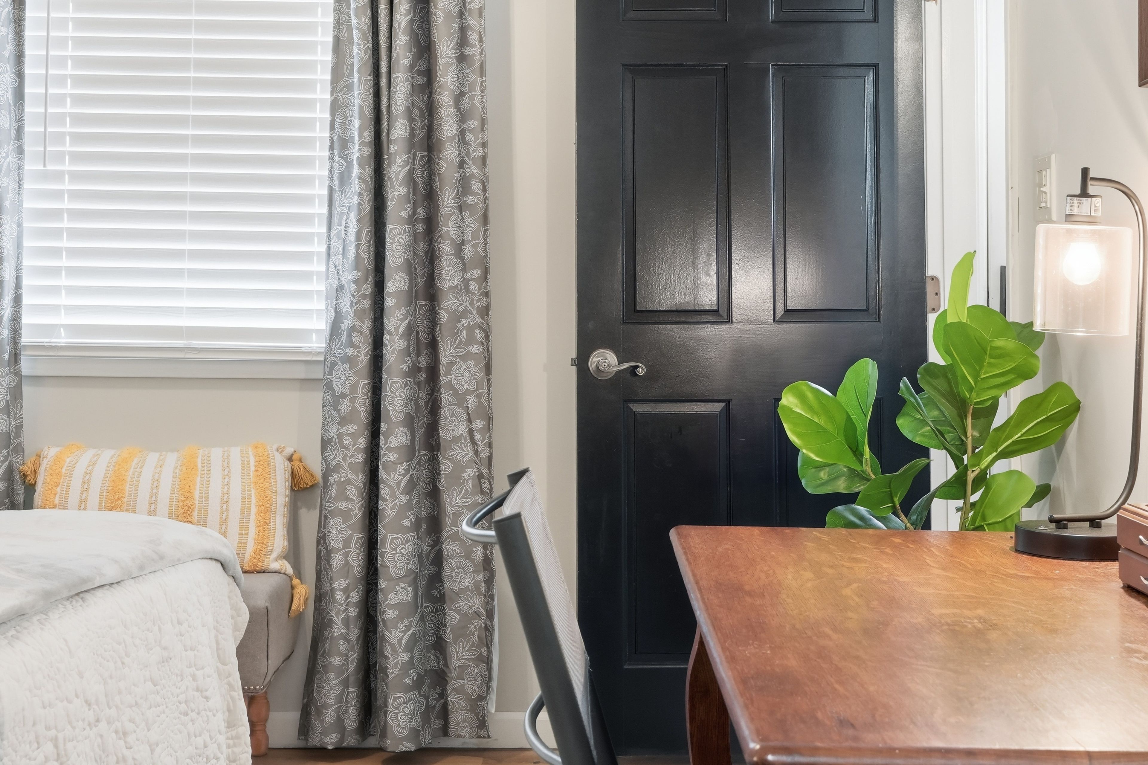 A room with a bed, a desk, a door, and a window with curtains.
