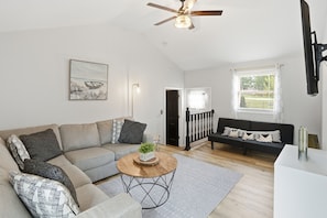 A modern living room with a sofa, a coffee table, and a ceiling fan. - Cedar Lake Sunrise: 1BR, 1.5 Bath with Lake View and Back Porch (Cedar Lake)